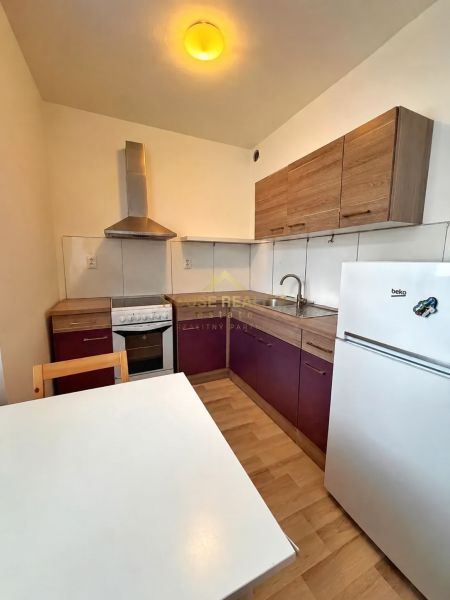 A kitchenette in a studio apartment with a corner unit, table, and wooden decor flooring.