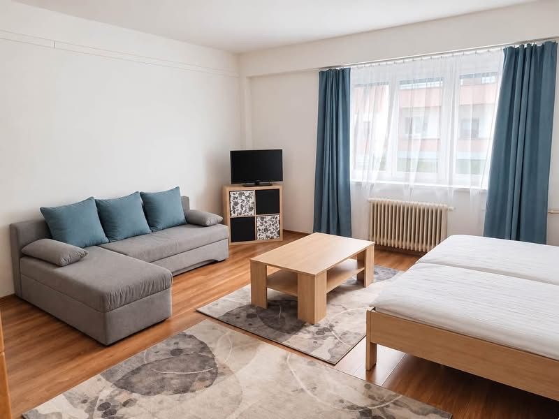 A one-room apartment with a sofa, bed, television, table, and floor with a wooden decor.