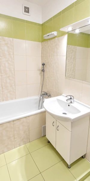 A bathroom in a studio apartment with a bathtub, a washbasin cabinet, and green tiles.