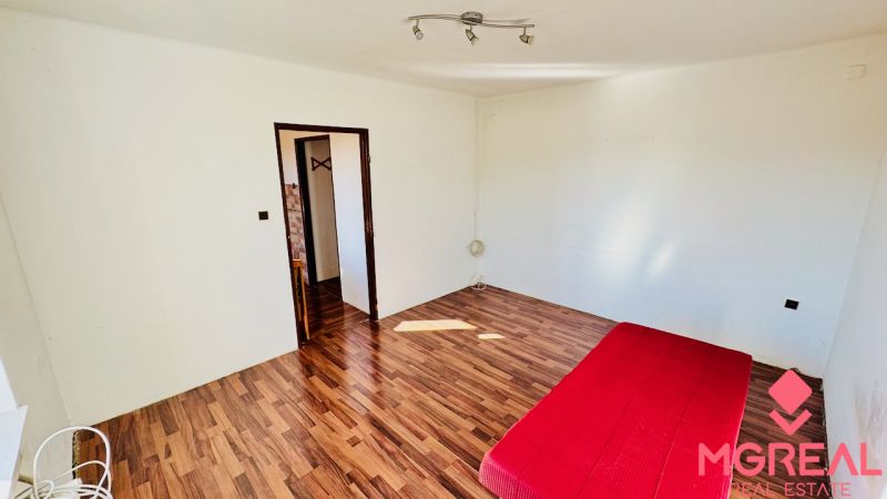 A room in a one-bedroom apartment with a red mattress and a wooden decor floor.