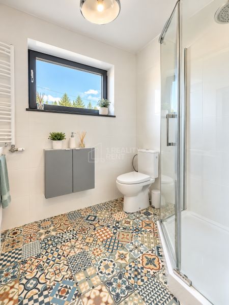 Bathroom with a shower, toilet, and window, colorful patterned tiles on the floor.