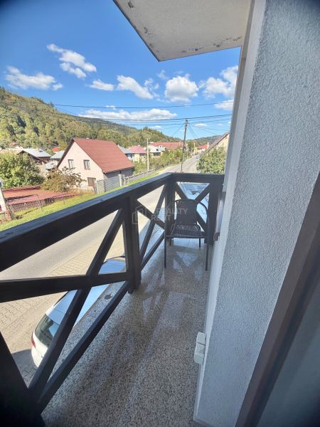 A balcony with a view of Centrum Street in Oščadnica, surrounded by greenery and houses, 1-room apartment.