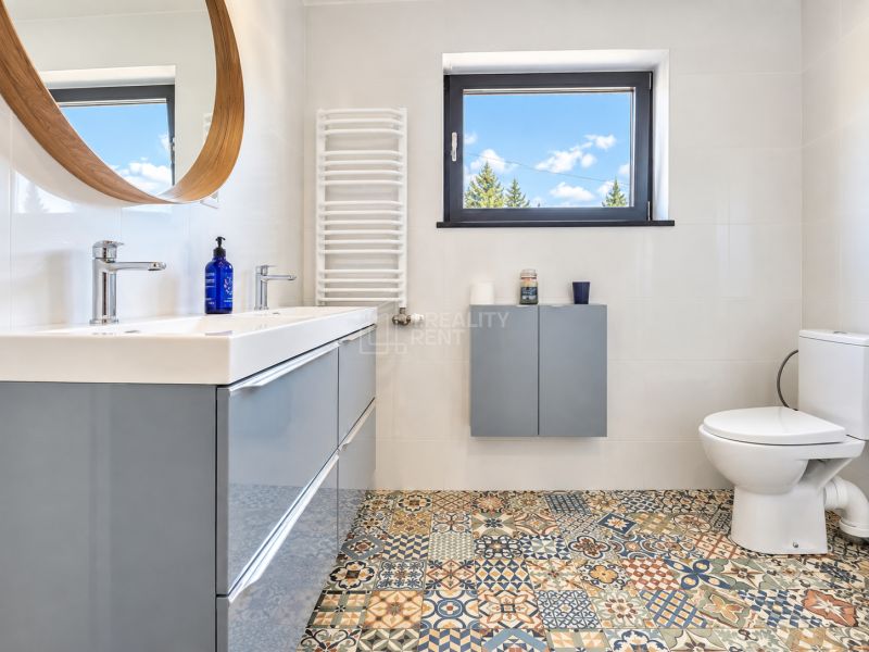 A bathroom with a mosaic floor, a modern sink, and a window in a studio apartment.