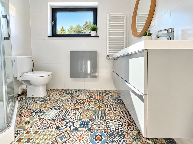 A bathroom with colorful tiles, a shower corner, and a mirror in a studio apartment.