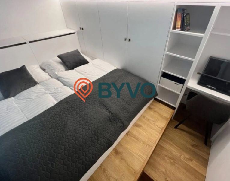 Bedroom in a studio apartment with a double bed and storage space, floor with wooden decor.