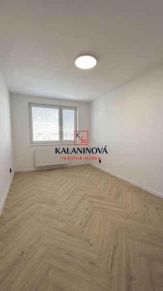A room with a wooden decor floor in a 4-room apartment elegantly illuminated by a large window.