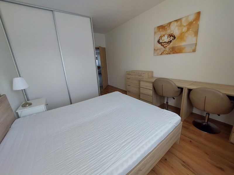 A bedroom with wood-patterned flooring, a bed, a desk, and wardrobes in a three-room apartment.