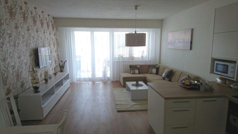 Living room in a three-room apartment with a wooden-patterned floor and floral wallpaper.