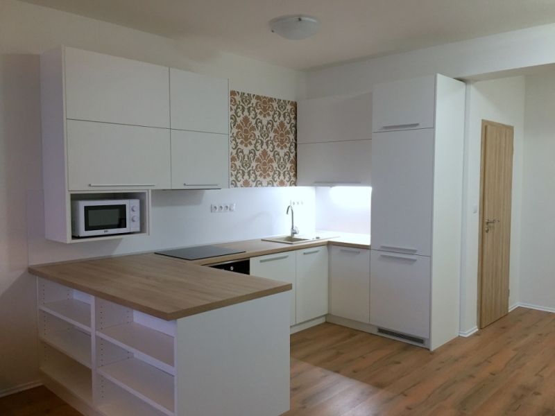 A kitchen with a white unit and a decorative wall in a three-room apartment, with a floor featuring a wood decor.