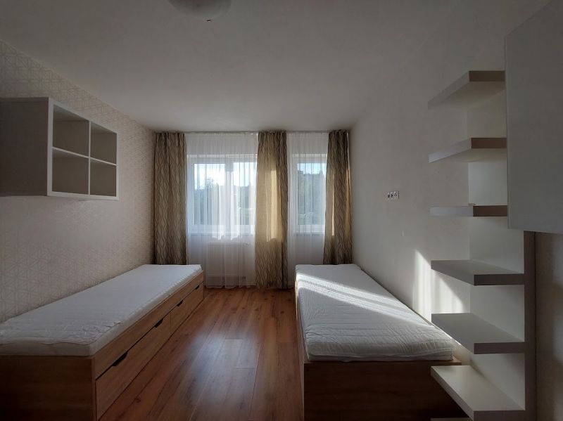 A room with two beds, shelves, and a floor with wooden decor in a three-room apartment.