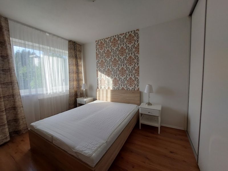 A bedroom with a bed, wallpaper, and a wooden decor floor in a 3-room apartment.