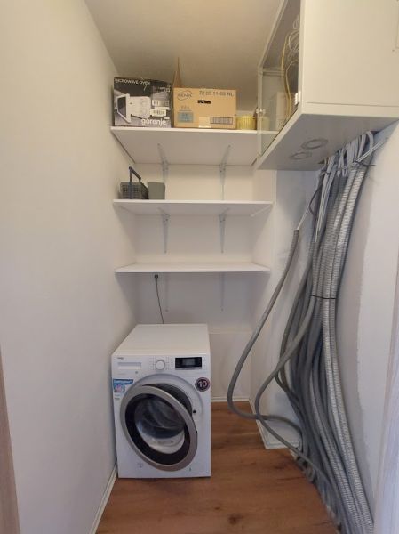 Utility room in a 3-room apartment with a washing machine and shelves, floor with wooden decor.