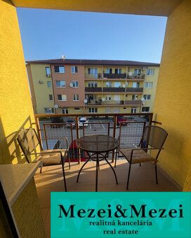 The balcony of a 2-room apartment in Vlčkovce with a table and chairs, view of the apartment building.