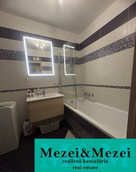 A bathroom with a mirror and a bathtub in a 2-room apartment; white tiles combined with mosaic.