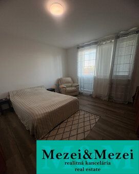 Bedroom in a 2-room apartment with a bed, chair, and wooden decor flooring.
