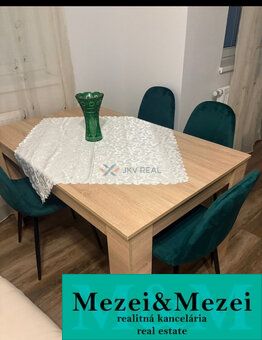 Dining table with a vase and green chairs, wooden decor flooring in a 2-room apartment.
