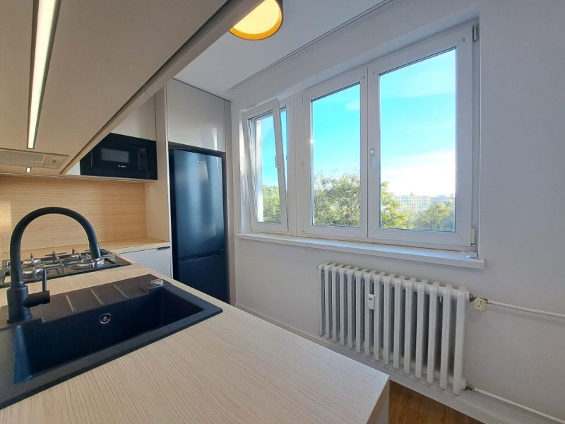 A kitchen in a 2-room apartment with a wood-patterned floor and large windows.