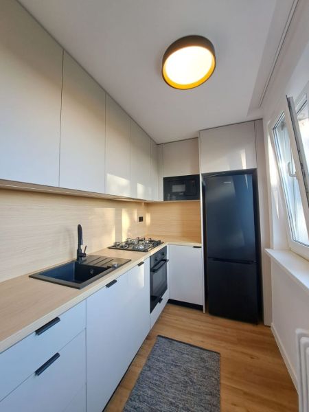 A kitchen in a 2-room apartment with white cabinets and a wood-patterned floor.