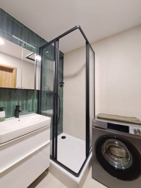 A bathroom of a 2-room apartment with a modern shower, a washing machine, and green tiles.