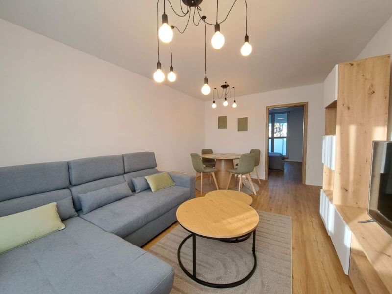 Living room with a sofa, wooden decor flooring, and a dining table in a two-room apartment.