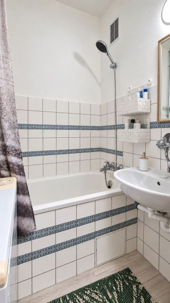 Bathroom with a bathtub, sink, white tiles, and patterned details in a 3-room apartment.