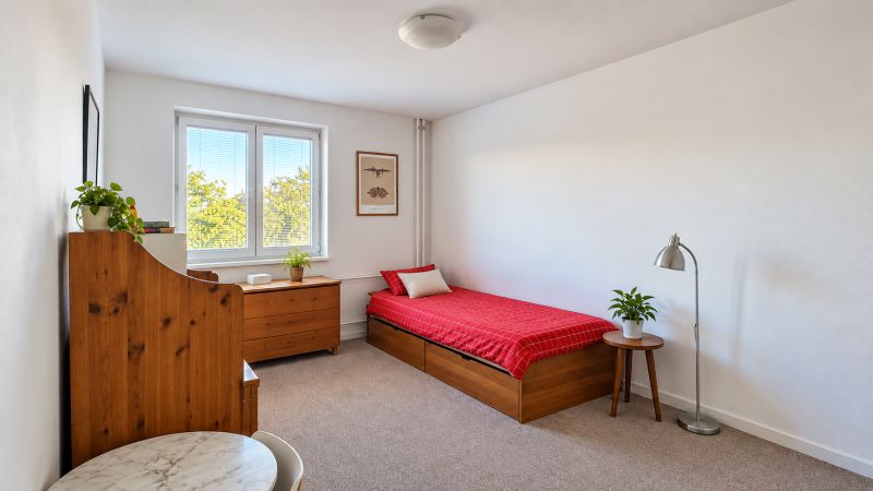A bright room in a 3-room apartment with a bed, a table, and wooden elements.
