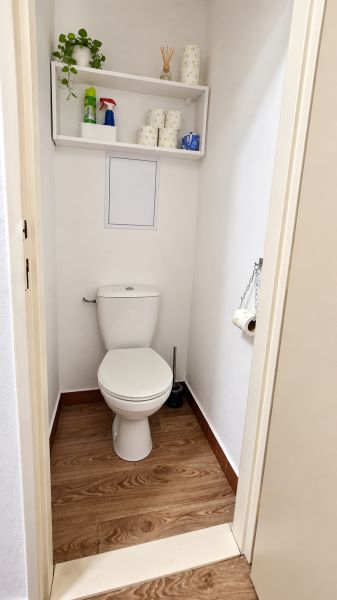 A toilet with a shelf and a wooden decor floor in a 3-room apartment.