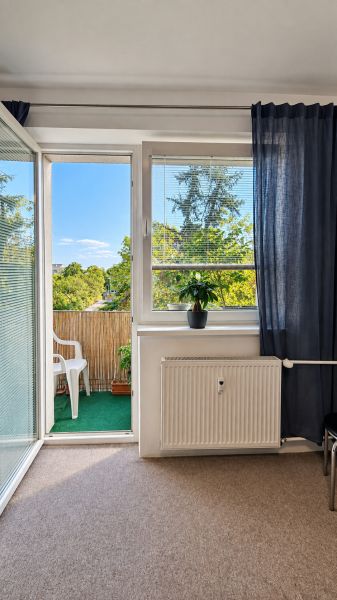 Living room in a three-room apartment with a view of the balcony and greenery.