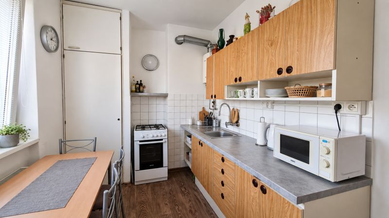 A kitchen in a 3-room apartment with a kitchen unit, appliances, and flooring with a wooden decor.
