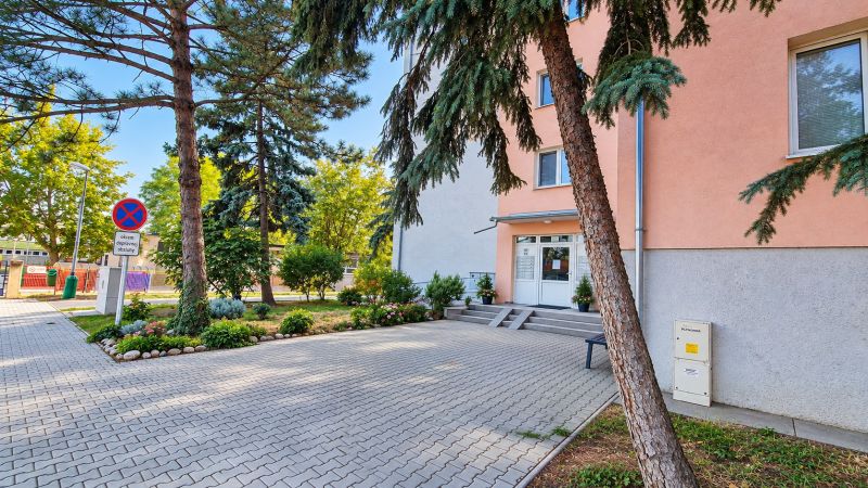 Entrance to a 3-room apartment in Pezinok on Za hradbami Street, surrounded by greenery and paving.