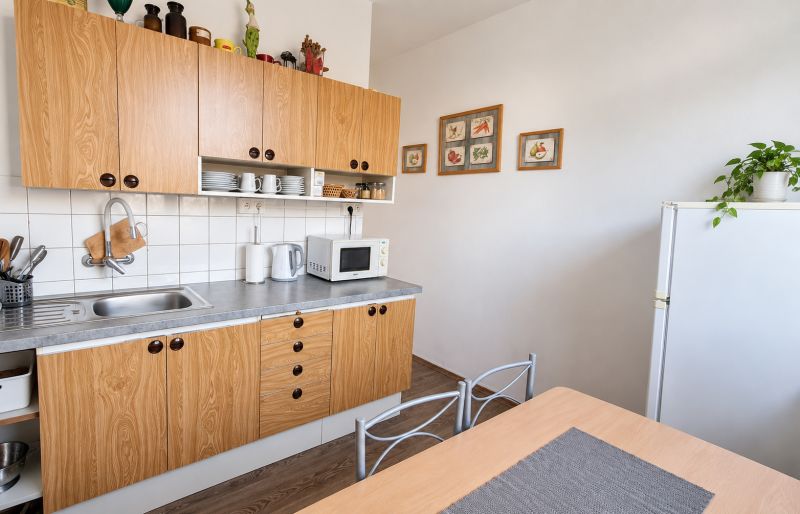 A kitchen in a 3-room apartment with a wood-patterned floor, white walls, and wooden cabinets.