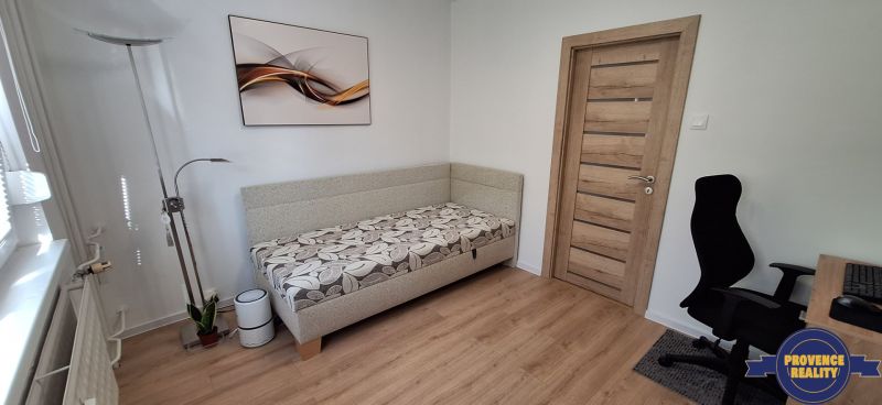A room in a 3-room apartment with a wooden decor floor, a sofa, and an office chair.