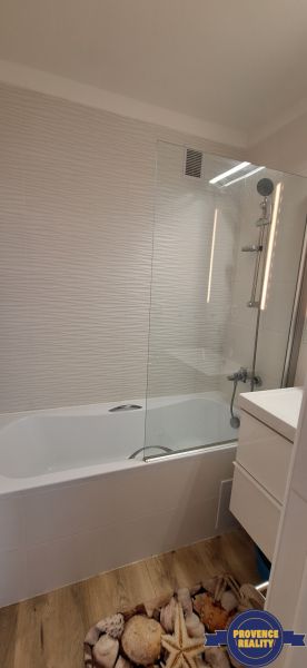 A bathroom in a 3-room apartment with a bathtub, white tiles, and a floor with a wooden decor.