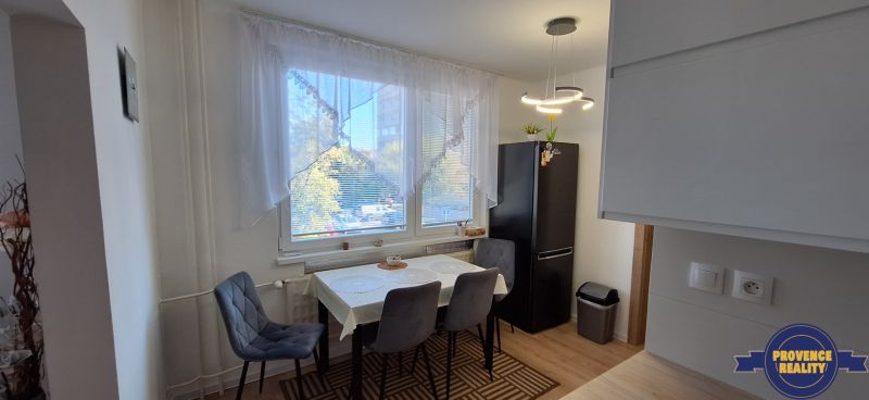 Dining area in a 3-room apartment with a dark refrigerator and wooden decor flooring.