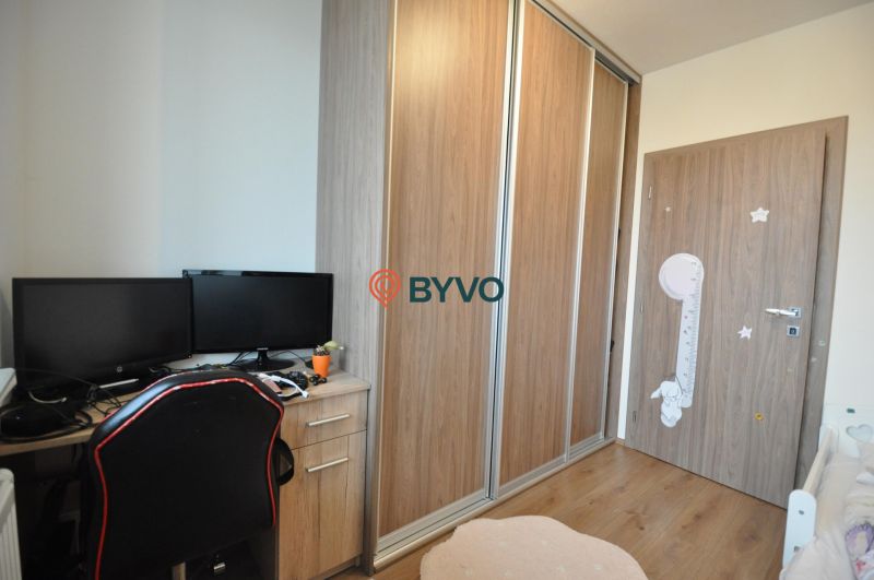 A workspace with a desk, two monitors, a wardrobe, and a wooden-patterned floor.