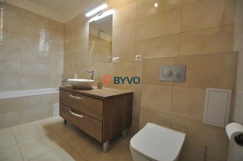 Bathroom with a bathtub, a sink on a wooden decor, and beige tiles in a 3-room apartment.