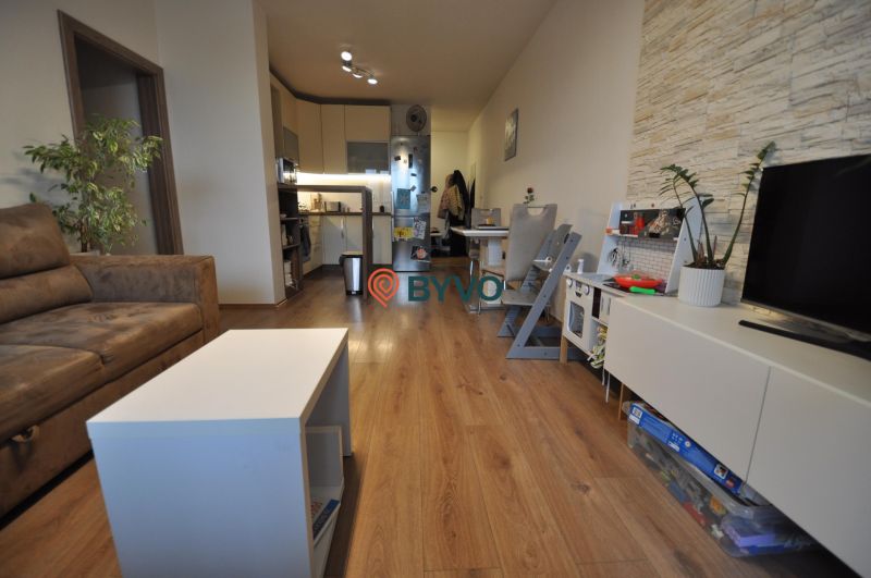 Living room in a three-room apartment with a wooden decor floor, a sofa set, and a kitchen.