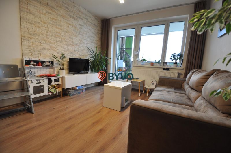 A living room in a three-room apartment with a wooden decor floor and stone cladding on the wall.
