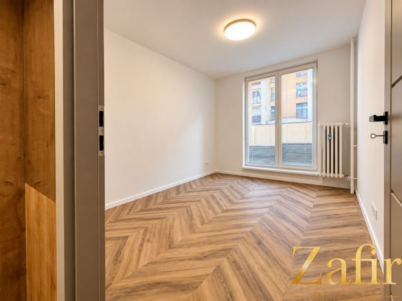 Interior of a 3-room apartment with wood-patterned flooring, white walls, large window.