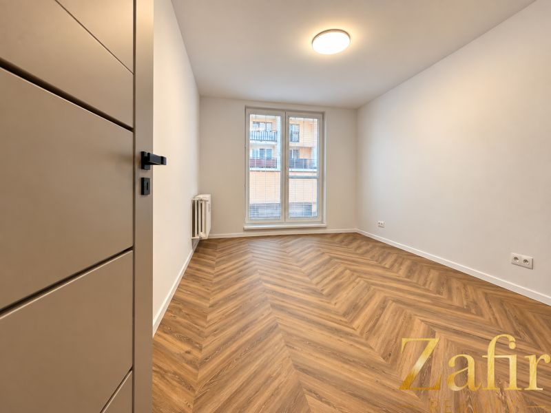 A room in a 3-room apartment with a wood-decor floor and a French window.