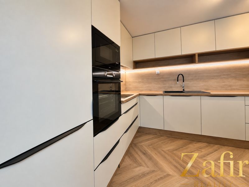 A kitchen unit with white cabinets and wooden decor in a 3-room apartment.