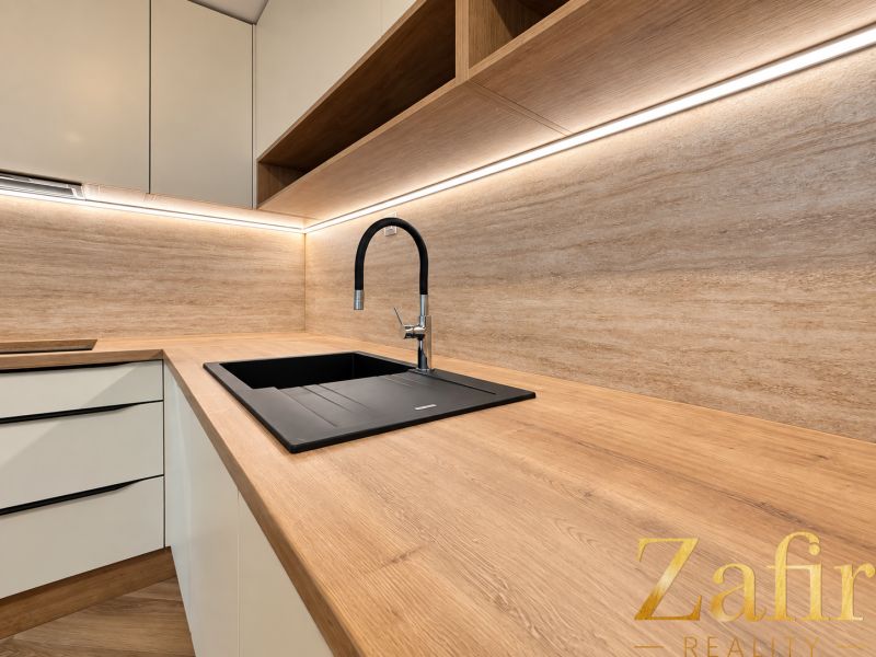 A kitchen in a 3-room apartment with a wooden decor floor and white cabinets.