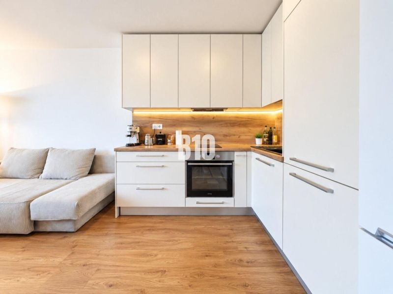 A kitchen in a 2-room apartment with a wood-patterned floor and white cabinets.