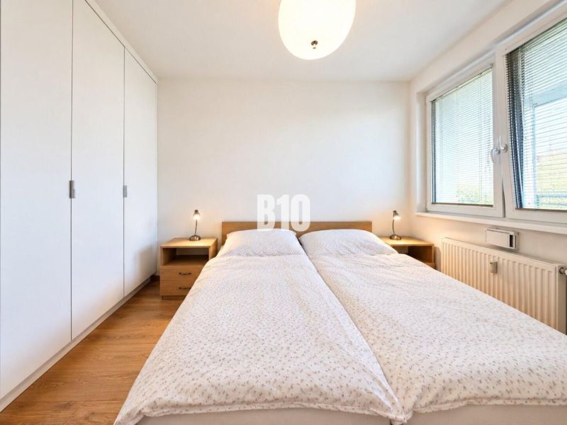 A bright bedroom with a large bed, wardrobe, and wood-decorated floor in a 2-room apartment.