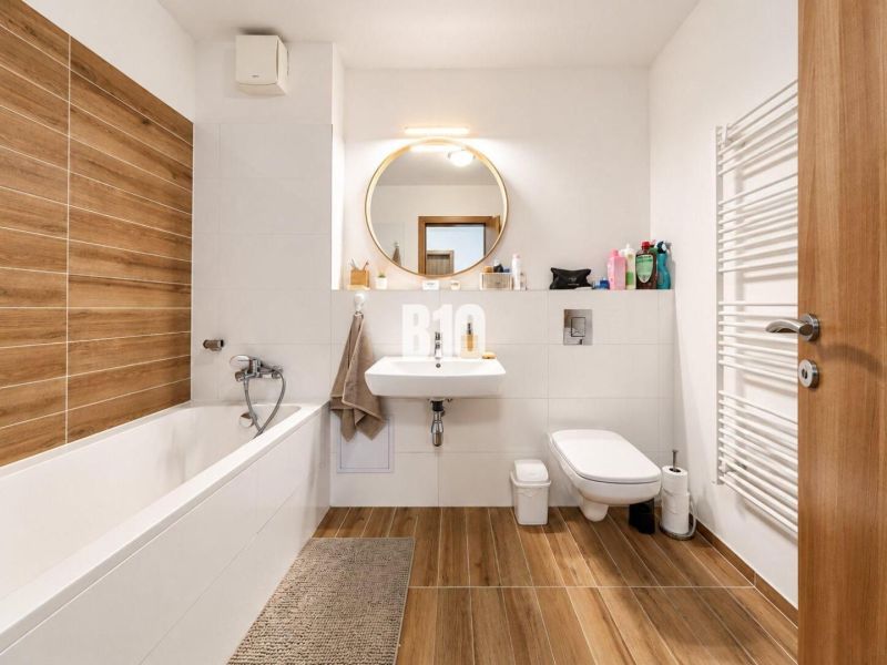 Bathroom in a 2-room apartment with a bathtub, sink, and floor with a wooden decor.