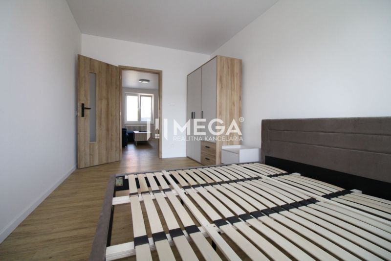 A bedroom in a two-room apartment with a wooden decor floor and simple furnishings.