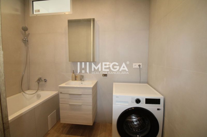 Bathroom in a 2-room apartment with a bathtub, washing machine, and floor with wood decor.