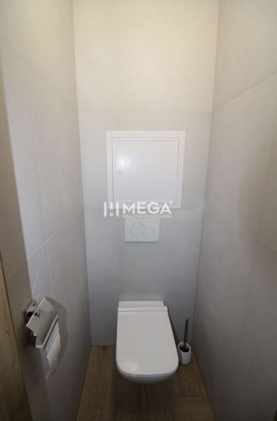 A toilet in a 2-room apartment with a wood-patterned floor and light-colored walls.