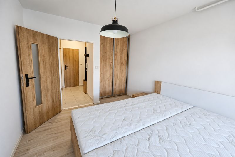 A bedroom in a 2-room apartment with a bed, wardrobe, and wooden decor flooring.