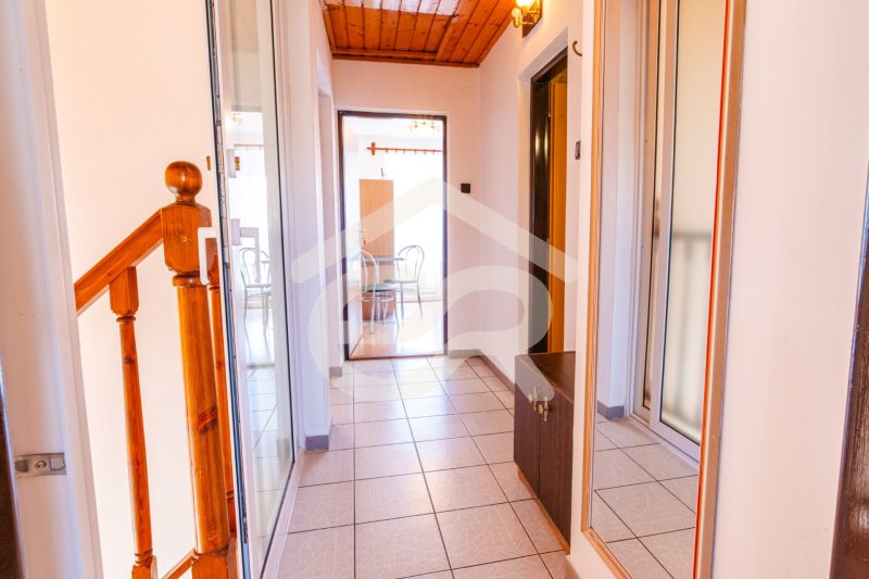 A hallway in a family house with tiles and a mirror, leading to a dining room with a wooden ceiling.